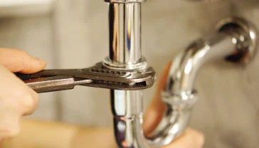 Plumber connecting a tap and drain pipe under a kitchen sink in a Dubai home