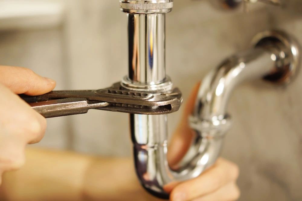 Plumber connecting a tap and drain pipe under a kitchen sink in a Dubai home